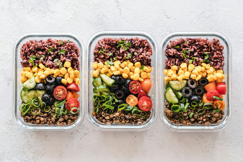 Drei Glasbehälter mit Reis, Mais, Oliven, Tomaten, Gurke und Linsen als Lunchbox