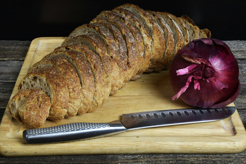 Körnerbrot, rote Zwiebel und Messer auf einem Holzbrett