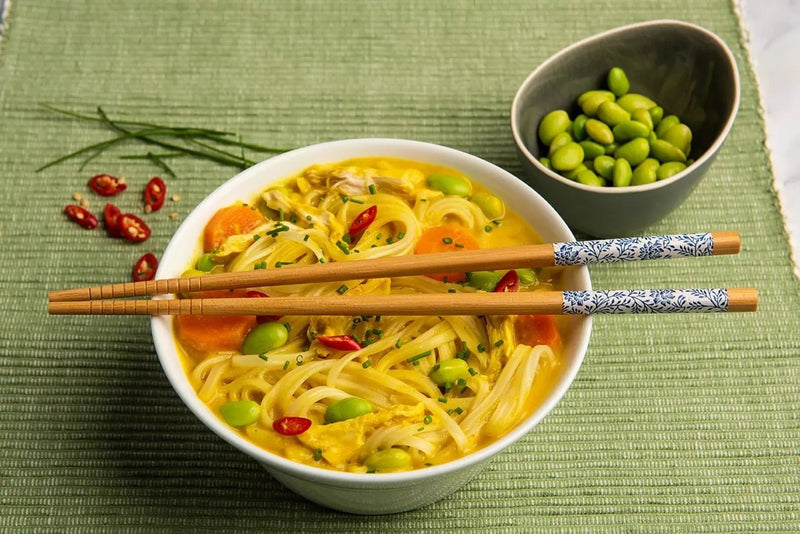 Katsu-Curry-Nudelsuppe mit Reisnudeln, Poulet, Karotten und Edamame, bestreut mit Schnittlauch und Chili