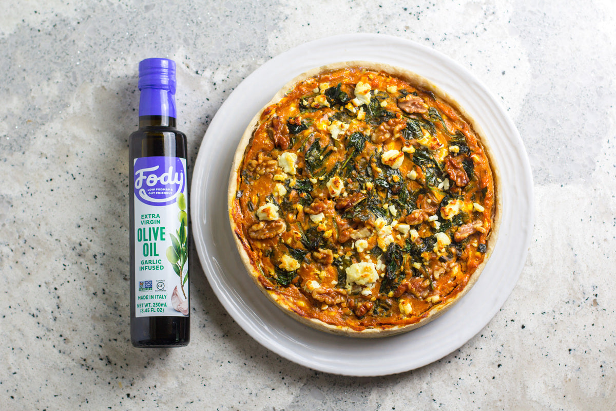 Fody Olivenöl mit Knoblauch-Aroma neben einer herzhaften Tarte auf weissem Teller.